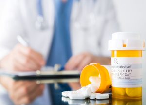 male-doctor-writing-on-a-clipboard-beside-prescription-medication-bottles